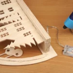 21-10-rehgefluester-schwibbogen-laubsaege-dekupiersaege-vorlage-lichterkette-einkleben-entlang-bogen-hinter-haeuserzeile-heissklebepistole